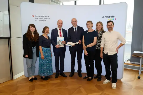 7 Personen mit Publikation in der Hand schauen in die Kamera