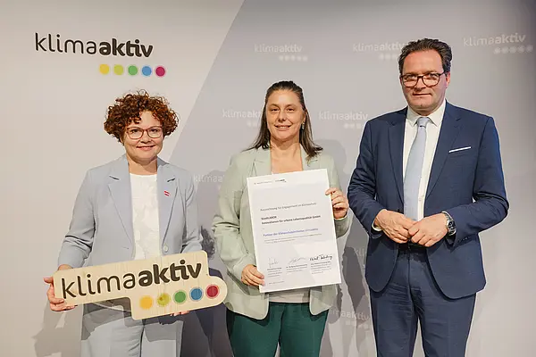 Menschen mit Urkunde und klimaaktiv Schild lächeln in die Kamera