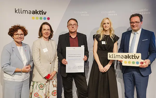 Menschen mit Urkunde und klimaaktiv Schild lächeln in die Kamera