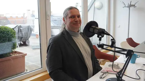 ein Mann vor einem Mikrofon lächelt in die Kamera