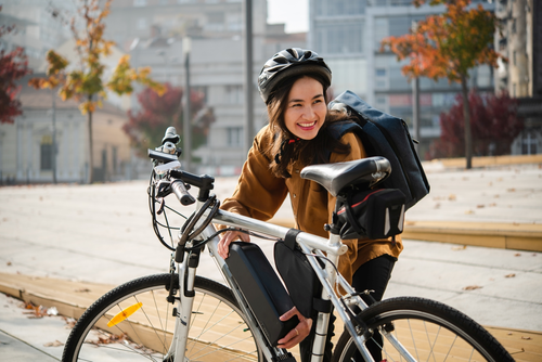 Frau tauscht gerade den Akku ihres E-Bikes. Sie trägt Helm und herbstliche Kleidung