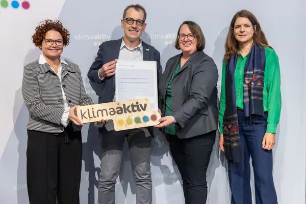4 Personen mit Urkunde und klimaaktiv Schild schauen in die Kamera
