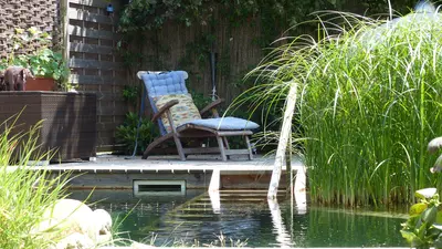 Ein Liegestuhl ist auf einem Steg daneben ist ein großer Teich.