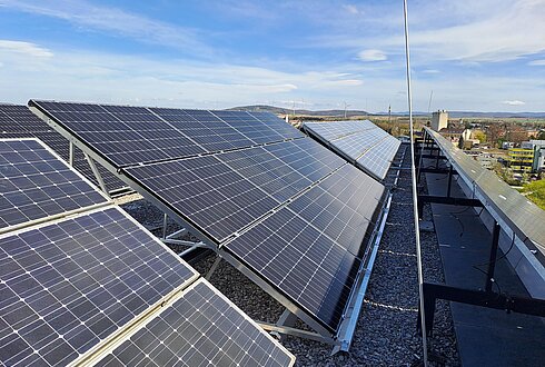 Schräg montierte Solarpaneele auf einem Kiesdach unter klarem, blauem Himmel.