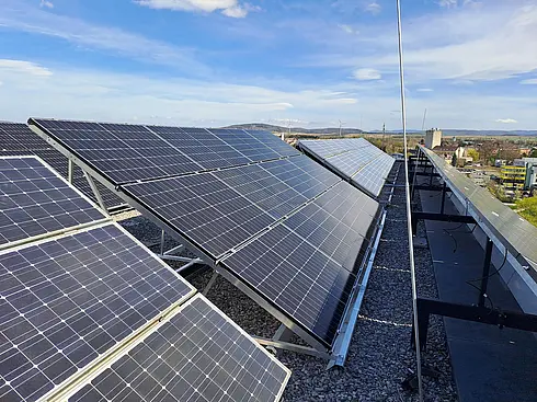 Schräg montierte Solarpaneele auf einem Kiesdach unter klarem, blauem Himmel.