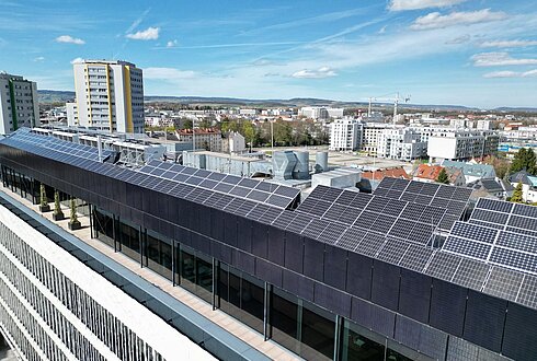 Luftbild eines langen Gebäudes mit Solarpaneelen auf dem Dach, angrenzend an eine Straße.