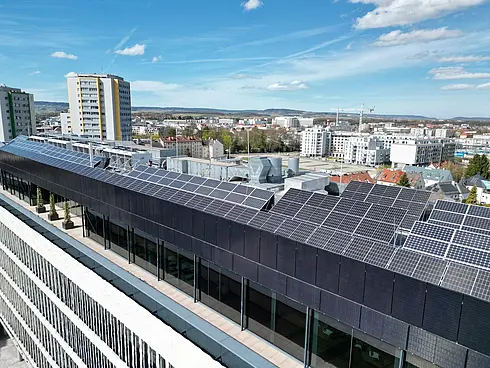 Luftbild eines langen Gebäudes mit Solarpaneelen auf dem Dach, angrenzend an eine Straße.