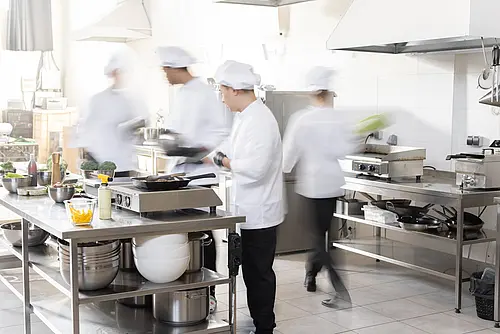 Chefkoch kocht in professioneller Küche. Köche beeilen sich und kochen aktiv Mahlzeiten für das Restaurant. Lange Belichtung mit Bewegungsunschärfe