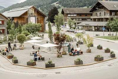Das Bild zeigt den Dorfplatz in Hittisau, der temporär als Pop-Up Maßnahme bekiest mit Sitzbänken und Pflanzen umgestaltet wurde