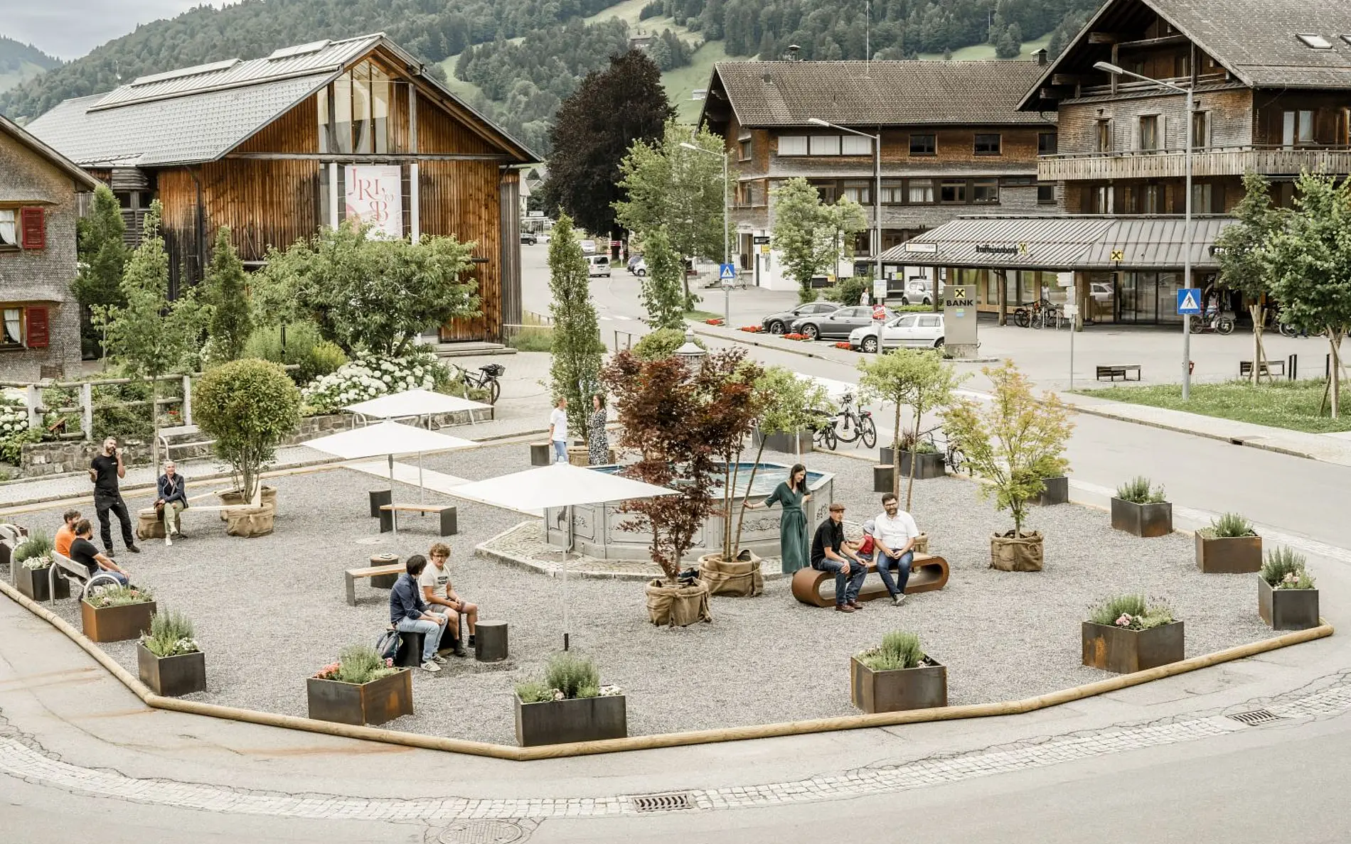 Das Bild zeigt den Dorfplatz in Hittisau, der temporär als Pop-Up Maßnahme bekiest mit Sitzbänken und Pflanzen umgestaltet wurde