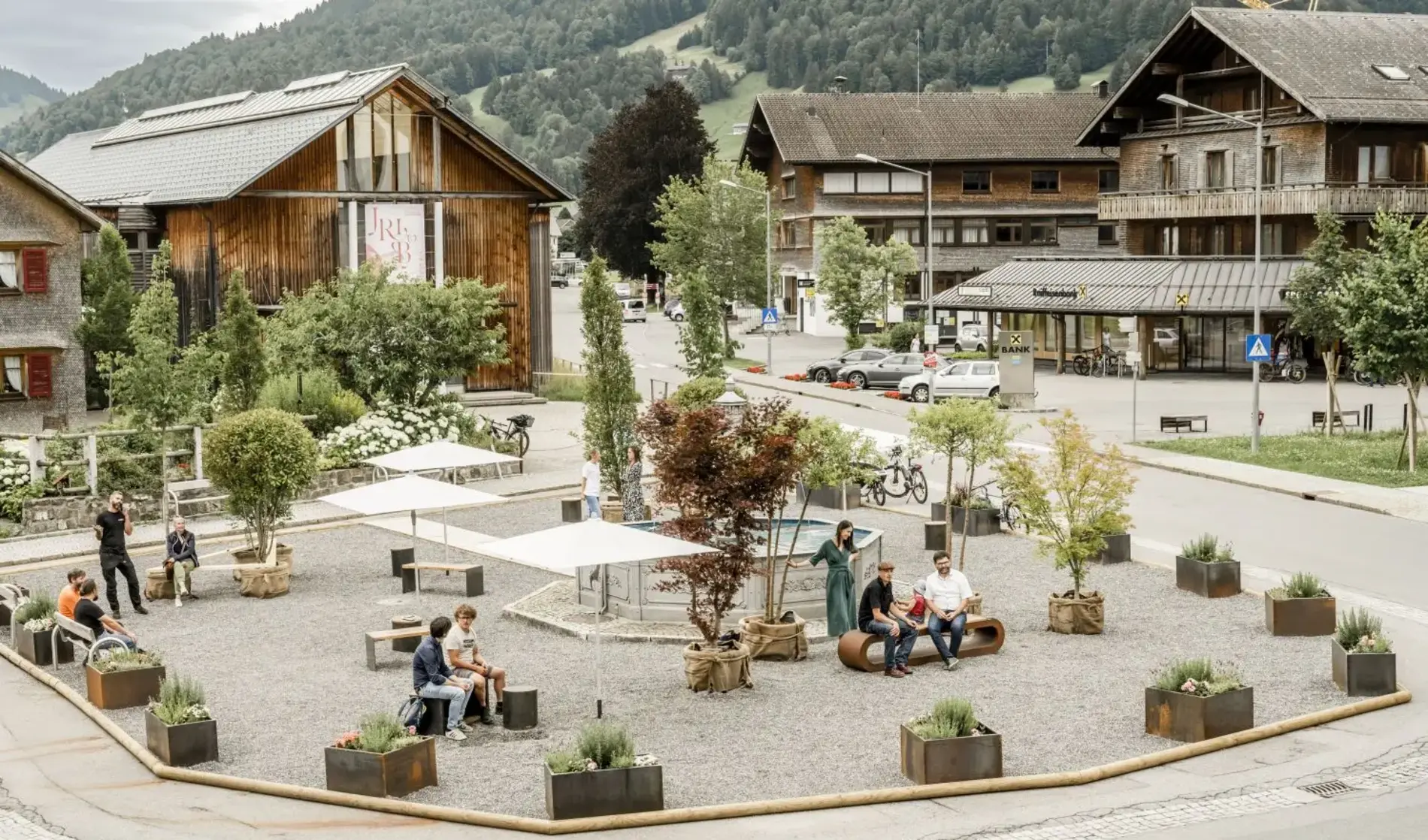Das Bild zeigt den Dorfplatz in Hittisau, der temporär als Pop-Up Maßnahme bekiest mit Sitzbänken und Pflanzen umgestaltet wurde
