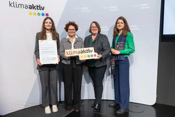 4 Personen mit Urkunde und klimaaktiv Schild schauen in die Kamera