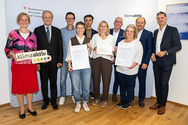 eine Gruppe von Menschen auf einer Bühne hält Urkunden in die Kamera
