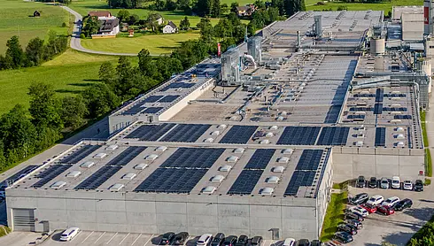 Nahaufnahme eines Fabrikdachs mit zahlreichen Photovoltaikmodulen und technischen Aufbauten.