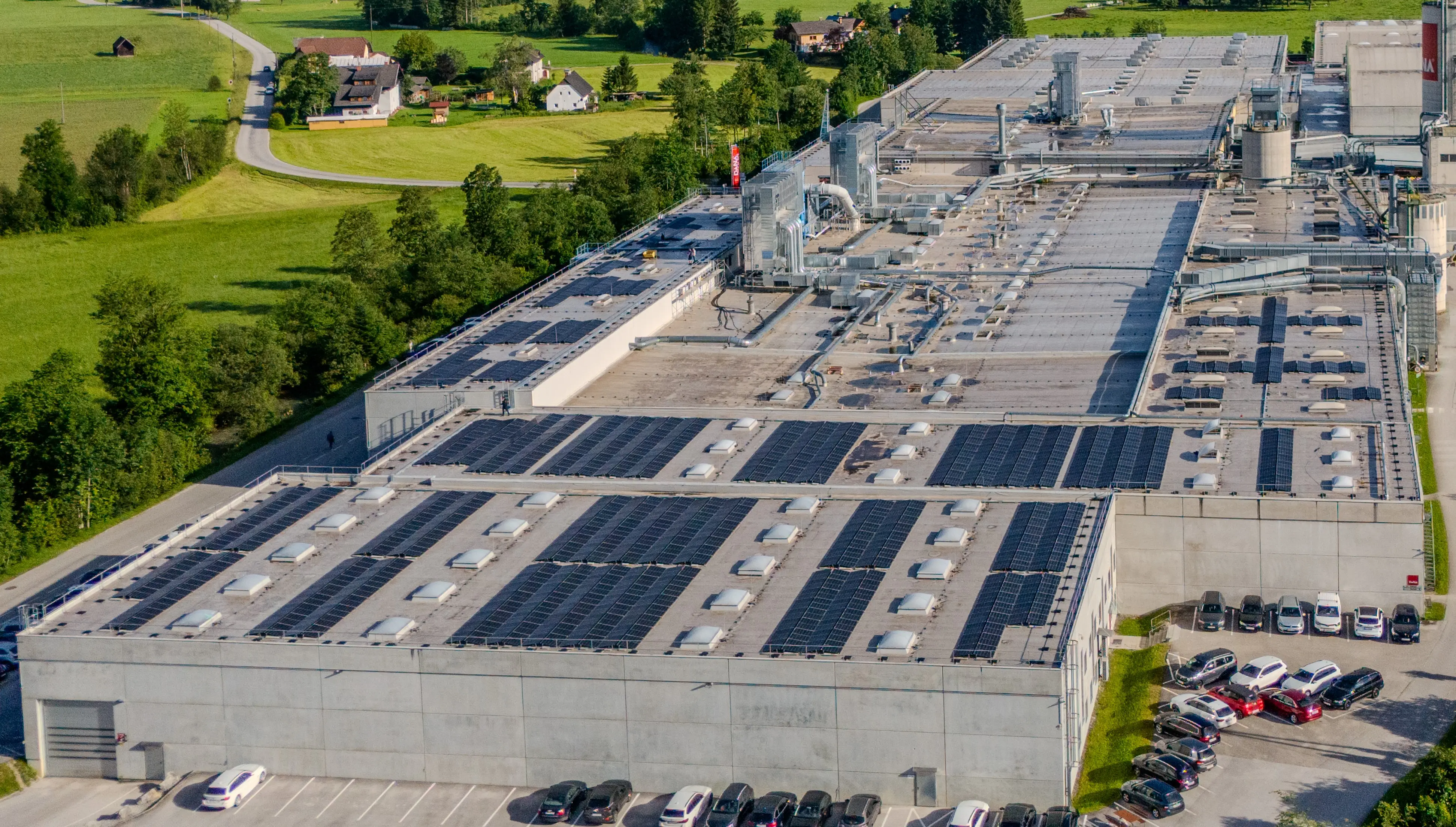 Nahaufnahme eines Fabrikdachs mit zahlreichen Photovoltaikmodulen und technischen Aufbauten.
