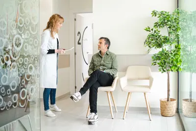 Ärztin spricht mit einem Patienten, der im Wartezimmer sitzt.