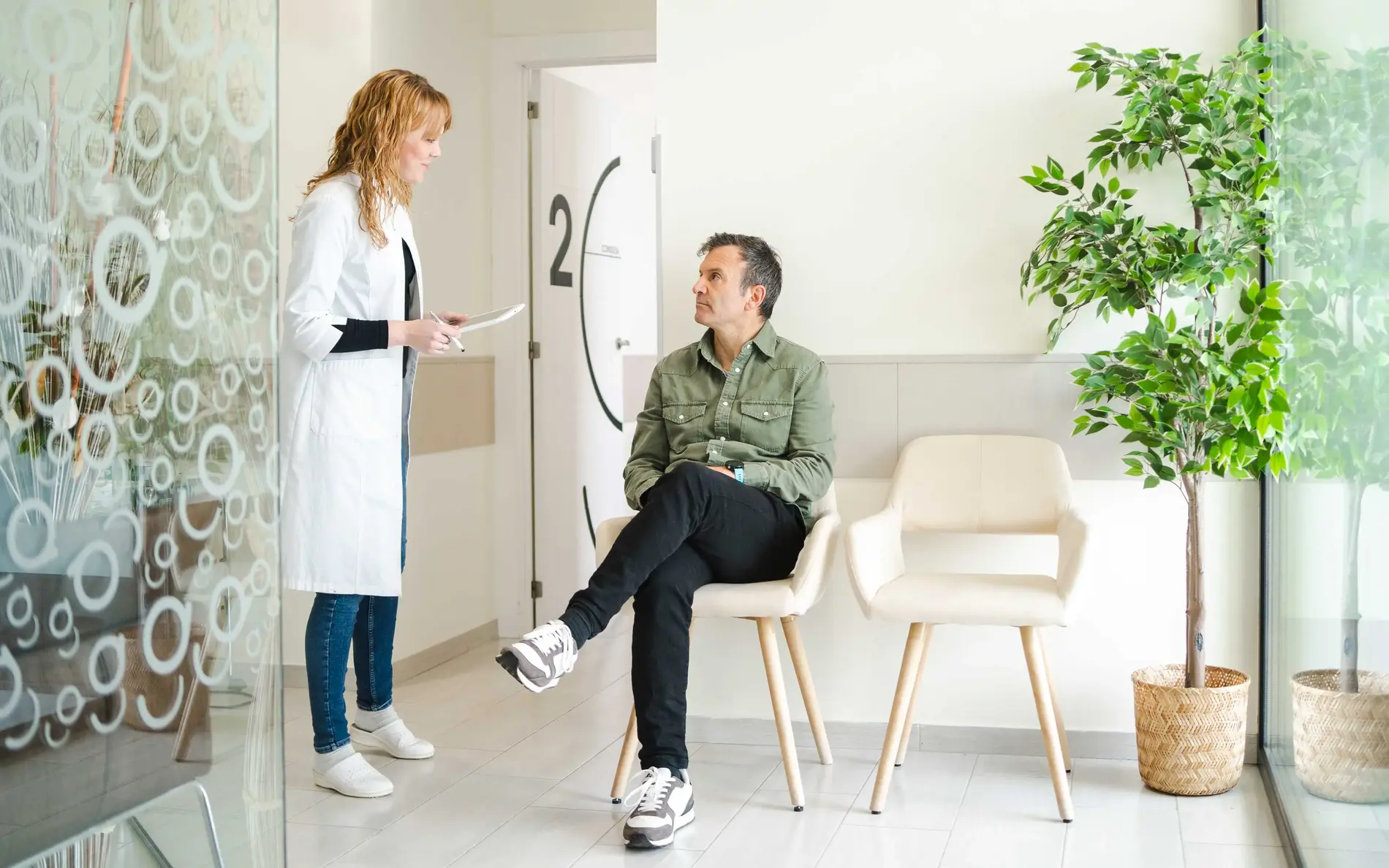 Ärztin spricht mit einem Patienten, der im Wartezimmer sitzt.