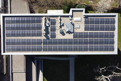 Luftaufnahme eines Daches mit mehreren Reihen von Solarpaneelen und technischen Einrichtungen.