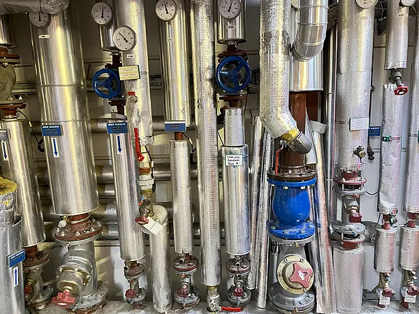 Komplexes Rohrsystem mit Ventilen, Druckanzeigen und Isolierung zur Rücklaufanhebung durch erhitztes Wasser von Kompressoren.