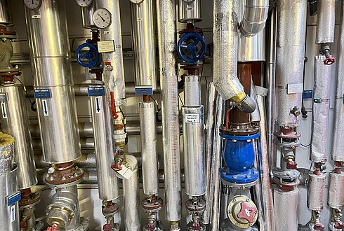 Komplexes Rohrsystem mit Ventilen, Druckanzeigen und Isolierung zur Rücklaufanhebung durch erhitztes Wasser von Kompressoren.