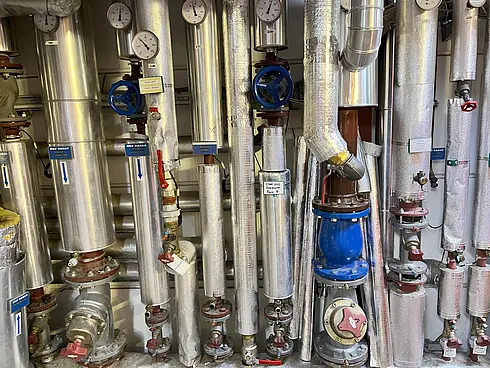 Komplexes Rohrsystem mit Ventilen, Druckanzeigen und Isolierung zur Rücklaufanhebung durch erhitztes Wasser von Kompressoren.