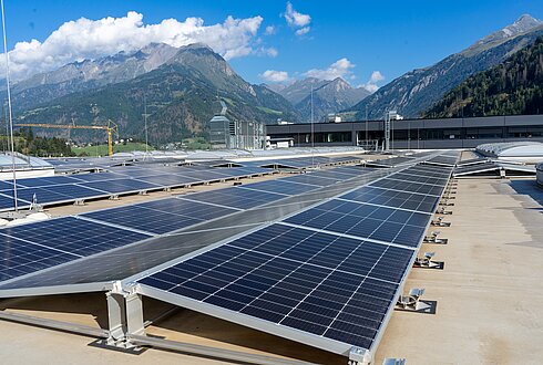 Solarpaneele auf einem Flachdach mit Blick auf Berge und blauen Himmel mit Wolken.