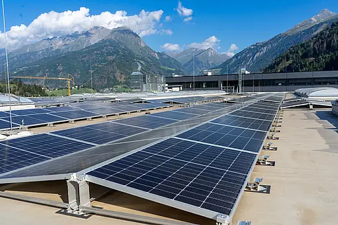 Solarpaneele auf einem Flachdach mit Blick auf Berge und blauen Himmel mit Wolken.