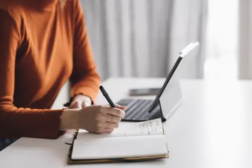 Eine Frau sitzt beim Schreibtisch und liest auf ihrem Laptop