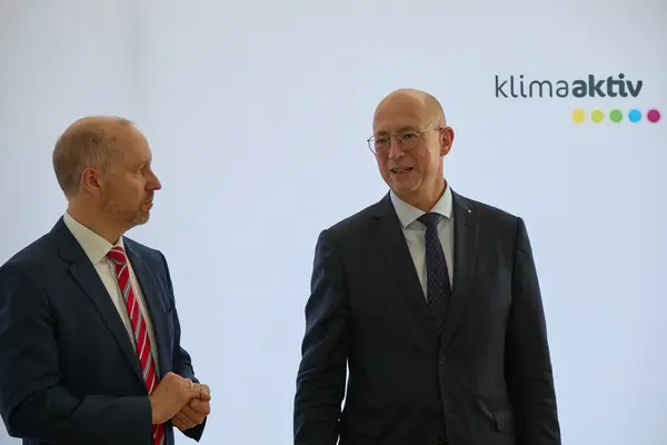 2 Männer in Anzug stehen vor einer Logowand klimaaktiv