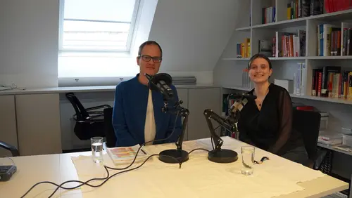 ein Mann und eine Frau vor Mikros lächeln in die Kamera