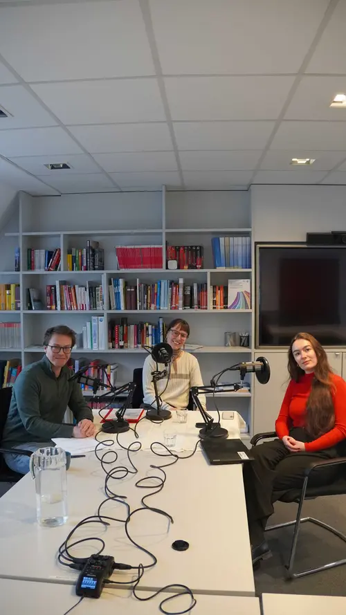 3 Personen vor Mikrofonen lächeln in die Kamera