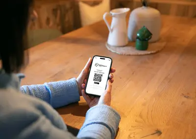 Eine Person hält ein Smartphone in den Händen, auf dem ein digitales Gästeticket mit QR-Code angezeigt wird. Der Bildschirm zeigt den Text 'Guest Mobility Ticket' sowie Gültigkeitsdaten.