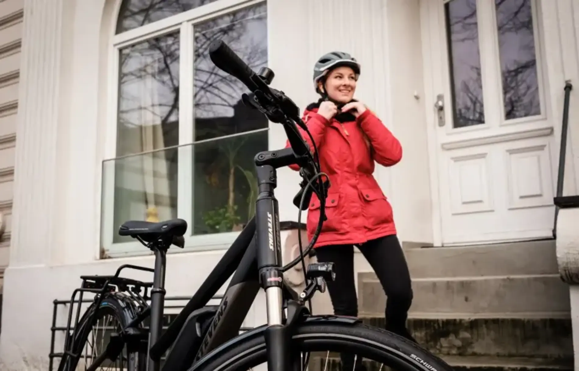 Eine junge Frau setzt sich gerade den Helm auf, vor ihr steht ein Fahrrad.