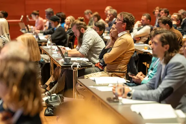 Mehrere Menschen sitzen entlang eines langen Tisches und blicken nach vorne zum Podium
