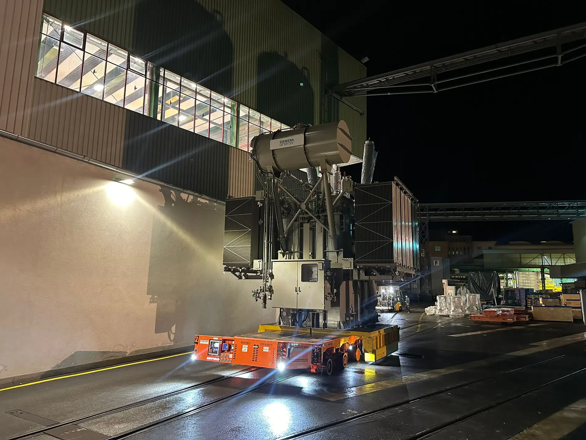 Schwerlasttransporter bewegt große Industriekomponente bei Nacht, beleuchtet durch starke Scheinwerfer.