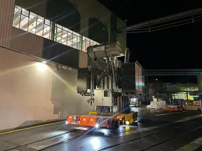 Schwerlasttransporter bewegt große Industriekomponente bei Nacht, beleuchtet durch starke Scheinwerfer.