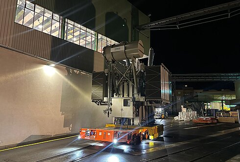 Schwerlasttransporter bewegt große Industriekomponente bei Nacht, beleuchtet durch starke Scheinwerfer.