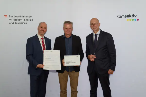 3 Personen mit Urkunde schauen in die Kamera