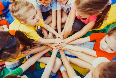 Kinder halten ihre Hände in die Mitte. Das Bild vermittelt Zusammenhalt