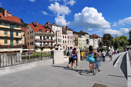 Menschen gehen zu Fuß und fahren mit dem Rad durch die Innenstadt Ljubljanas bei sommerlichen Wetter.