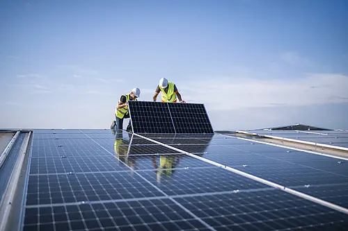 Zwei Männer in Baustellenmontur legen gerade ein Solarpanel zur restlichen PV-Anlage