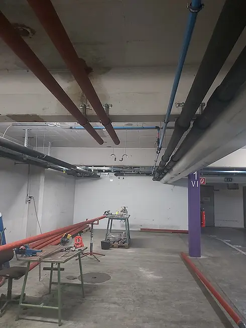 Mehrere farbige Rohrleitungen verlaufen entlang einer Betonwand in einem technischen Installationsbereich.