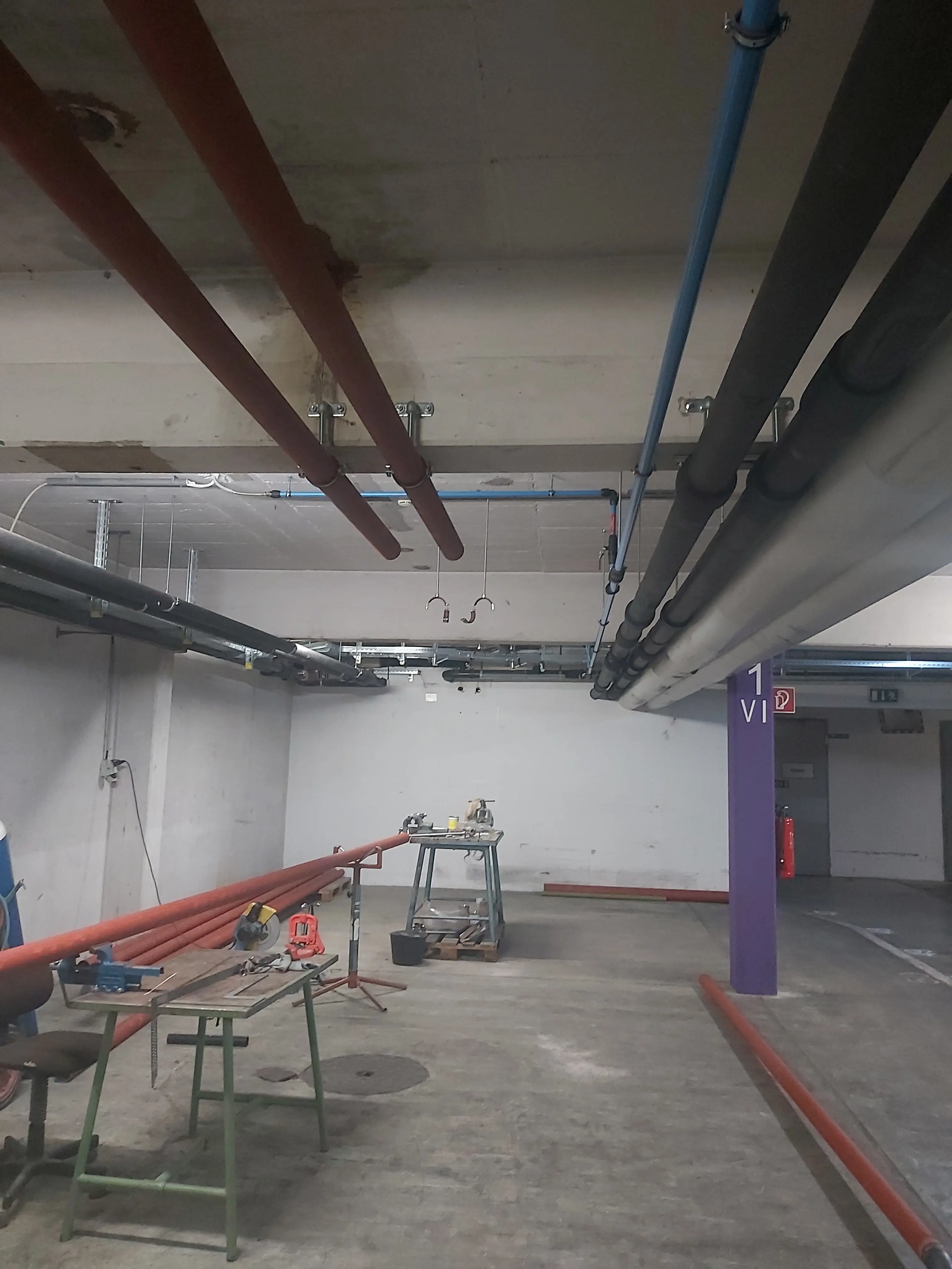 Mehrere farbige Rohrleitungen verlaufen entlang einer Betonwand in einem technischen Installationsbereich.