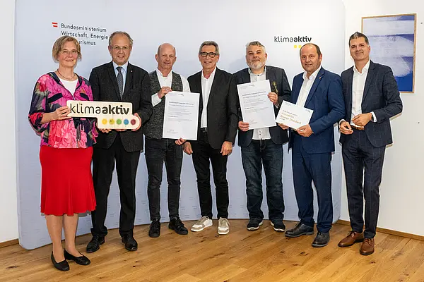 eine Gruppe von Menschen auf einer Bühne hält Urkunden in die Kamera