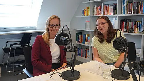 zwei Frauen sitzen vor einem Podcast Mikrofon
