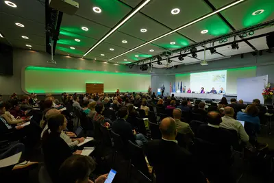 Großer Saal mit vielen Sitzplätzen und Telinehmer:innen mit Blick auf die Bühne
