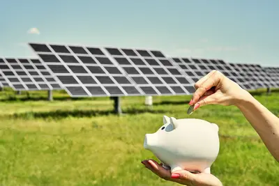 eine Frauenhand wirft Geld in ein Sparschwein, im Hintergrund Agri-PV