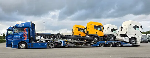 Blauer Sattelschlepper transportier auf langem Anhänger einen gelben und einen weißen Sattelschlepper