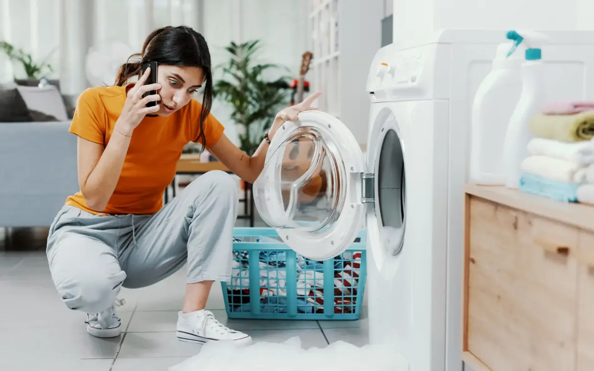 Eine Frau hockt verdutzt vor ihrer offenen Waschmaschine und telefeniert.