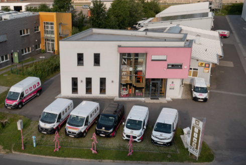 Gebäude der Firma Stanzl mit mehreren Firmenfahrzeugen vor dem Eingang, aufgenommen aus erhöhter Perspektive.